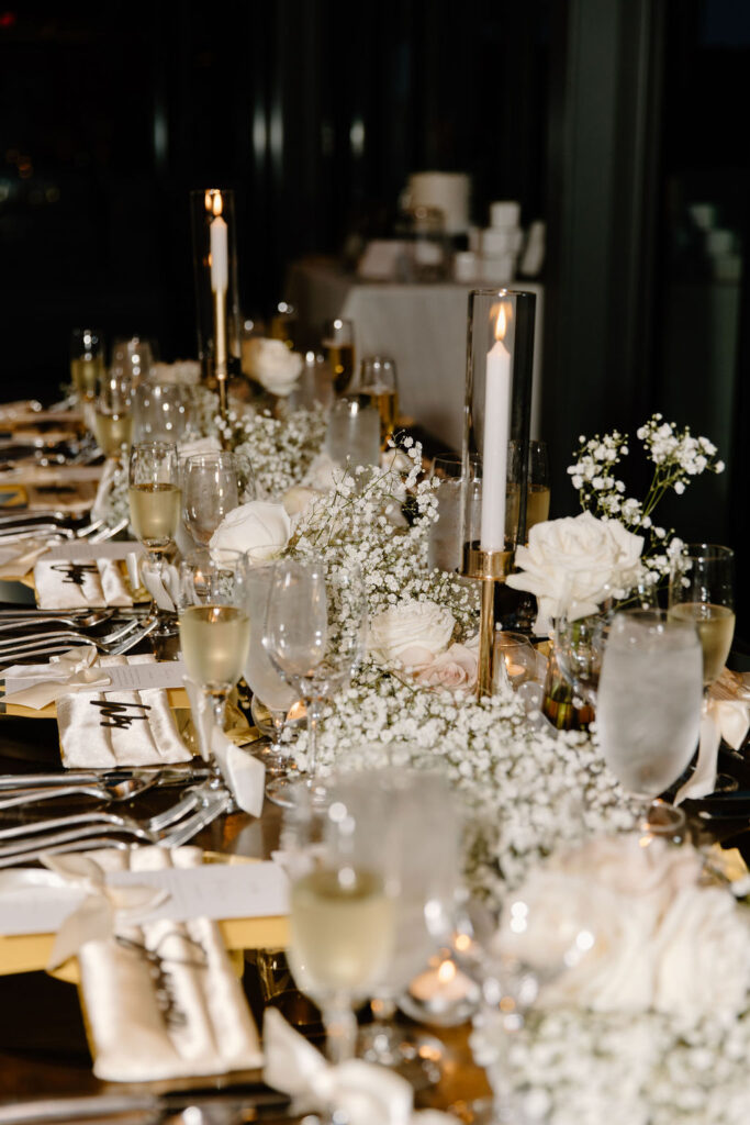 Long reception table decor with white taper candles, baby's breath, and white roses.