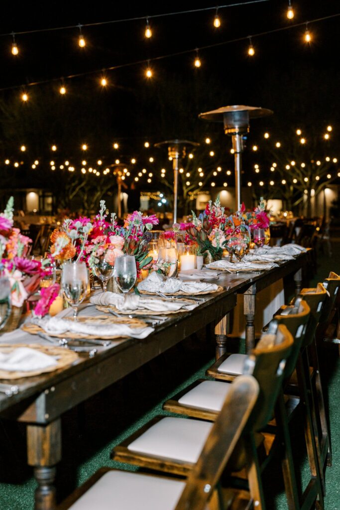 Nighttime wedding reception long rectangular table with candles and floral centerpieces down center of place settings.