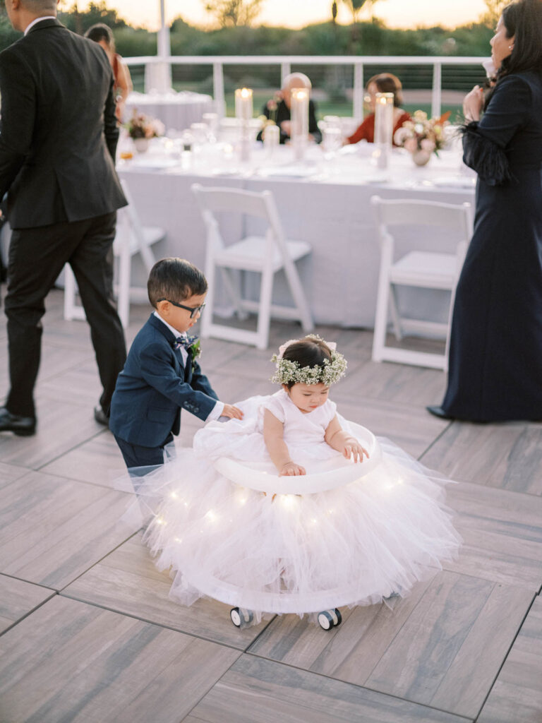 Ring bearer pushing flower girl in tulle decorated walker around wedding reception floor.