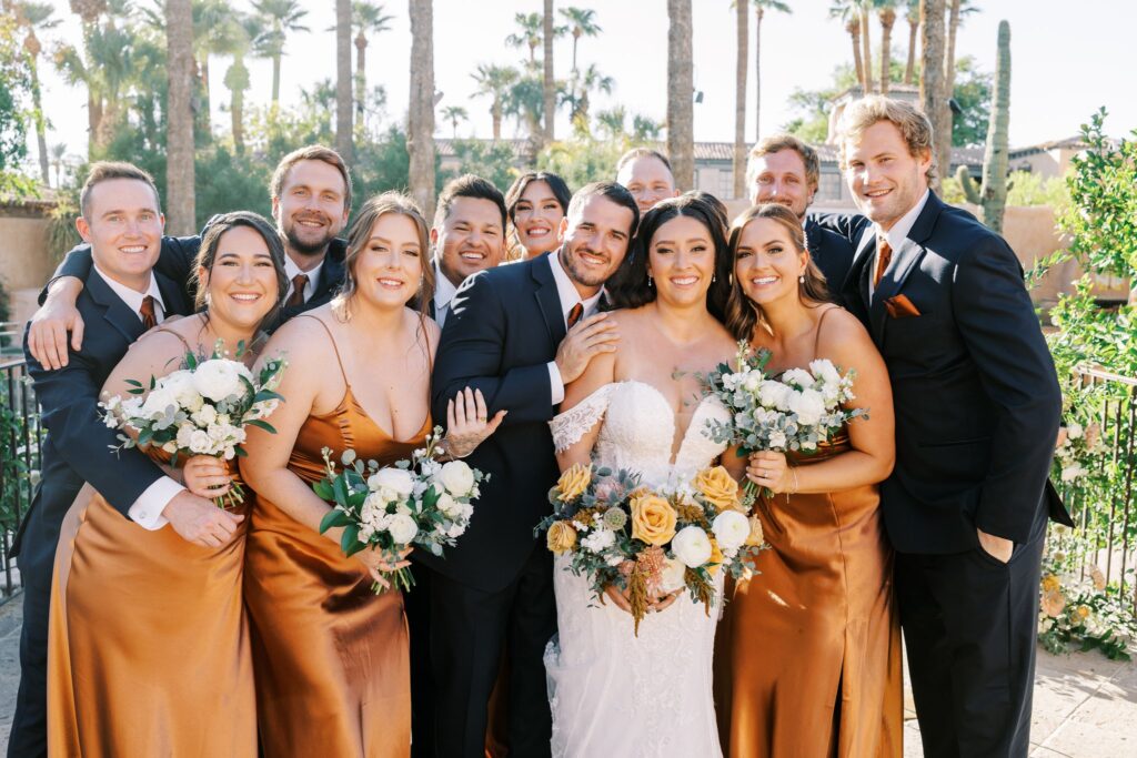 Bride and groom standing with wedding party, all close together and smiling.