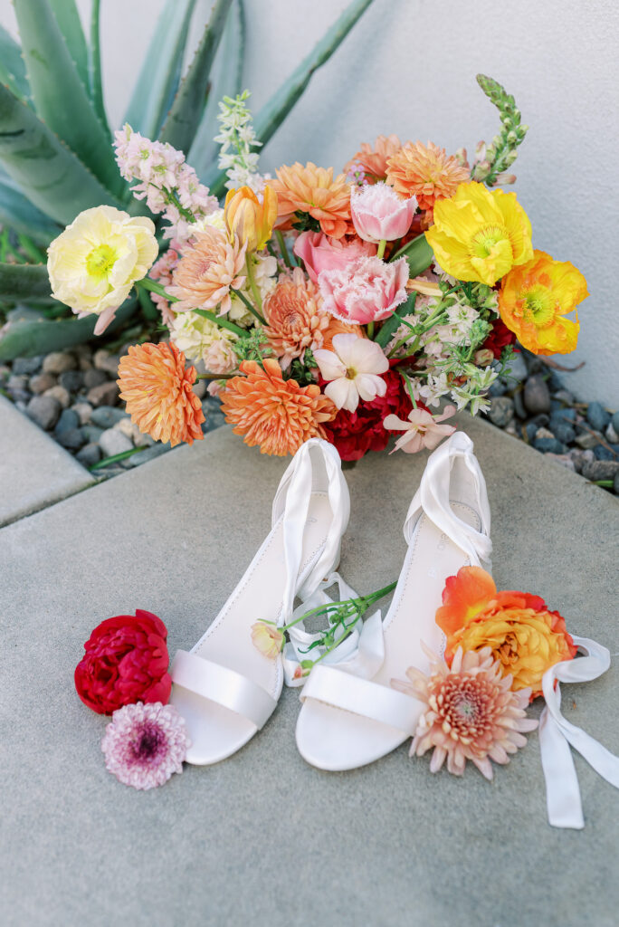 Bridal shoes with colorful flowers and bridal bouquet on ground.