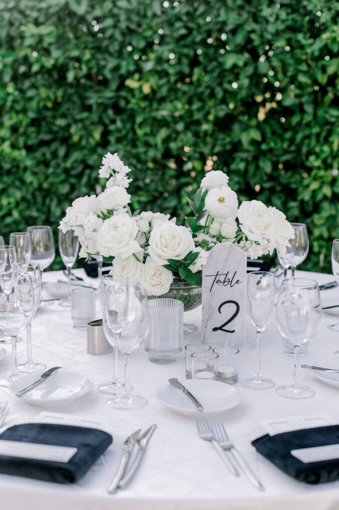 Wedding reception centerpiece of white flowers and greenery in glass vase.