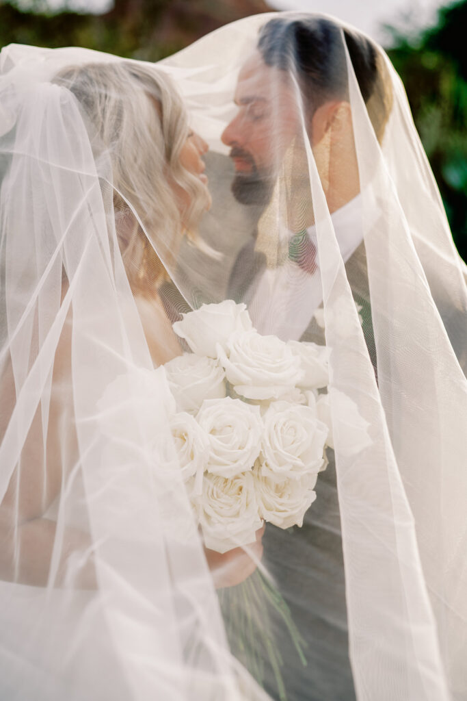 Bride and groom standing close, looking at each other with veil draped over them.