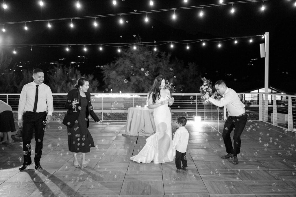 Bride and groom dancing with other guests and ring bearer at wedding reception with bubbles all around them.