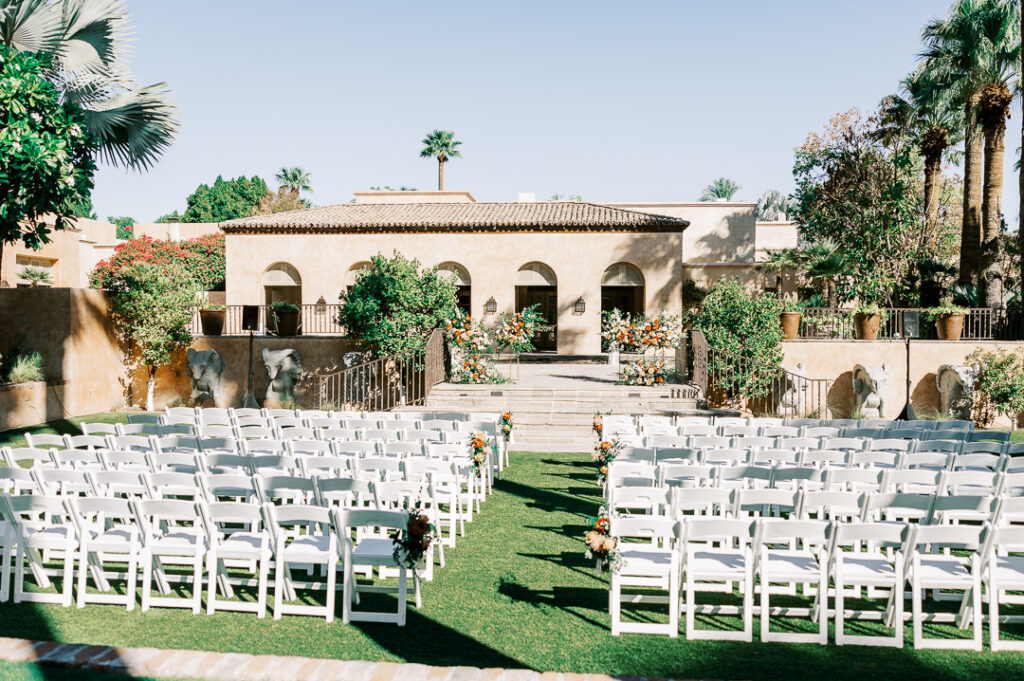 Outdoor wedding ceremony at Royal Palms resort with white chairs for guests and floral designs added to some aisle chairs as well as altar space.