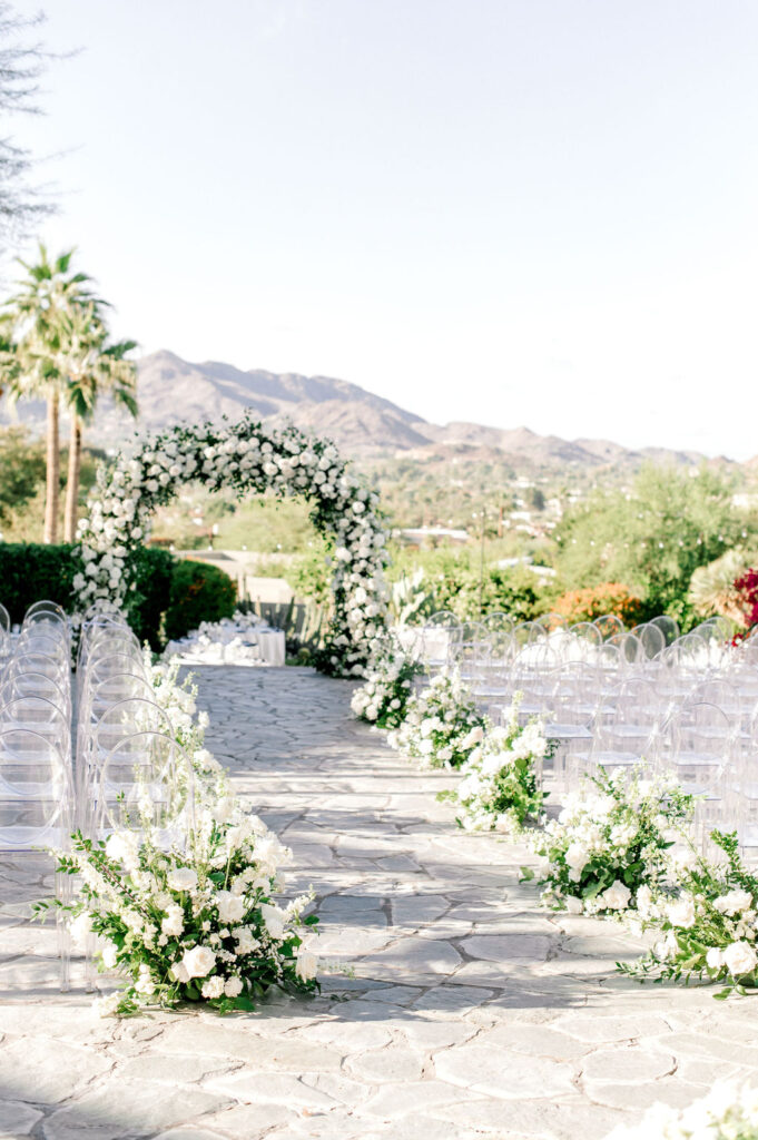 Outdoor wedding ceremony with white flowers and greenery aisle arrangements.