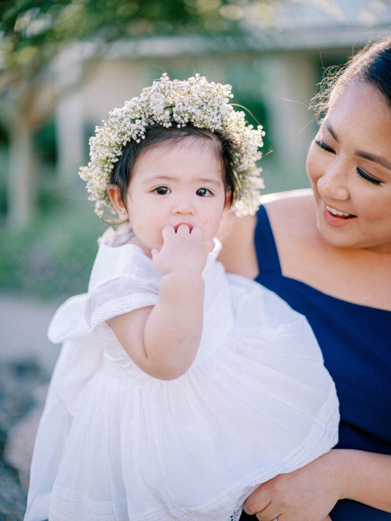 Woman holding flower girl in white dress with a baby's breath crown on.