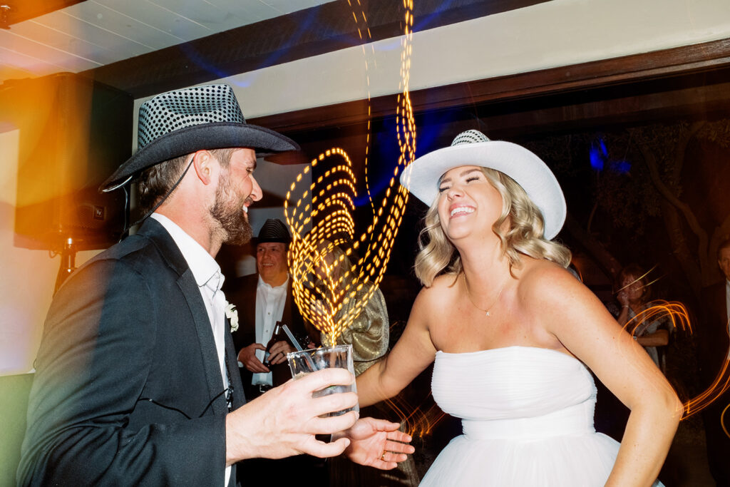 Overexposed photograph of bride and groom dancing during wedding reception with cowboy hats on.