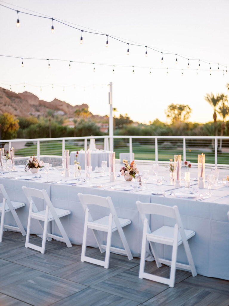 Long reception table with light gray linen, taper candles, bud vases of floral, and floral centerpieces.