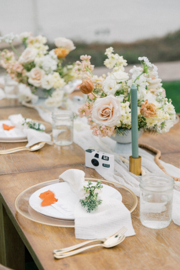 Wedding reception place settings with sage taper candles and pink, white, yellow and peach flowers centerpieces.