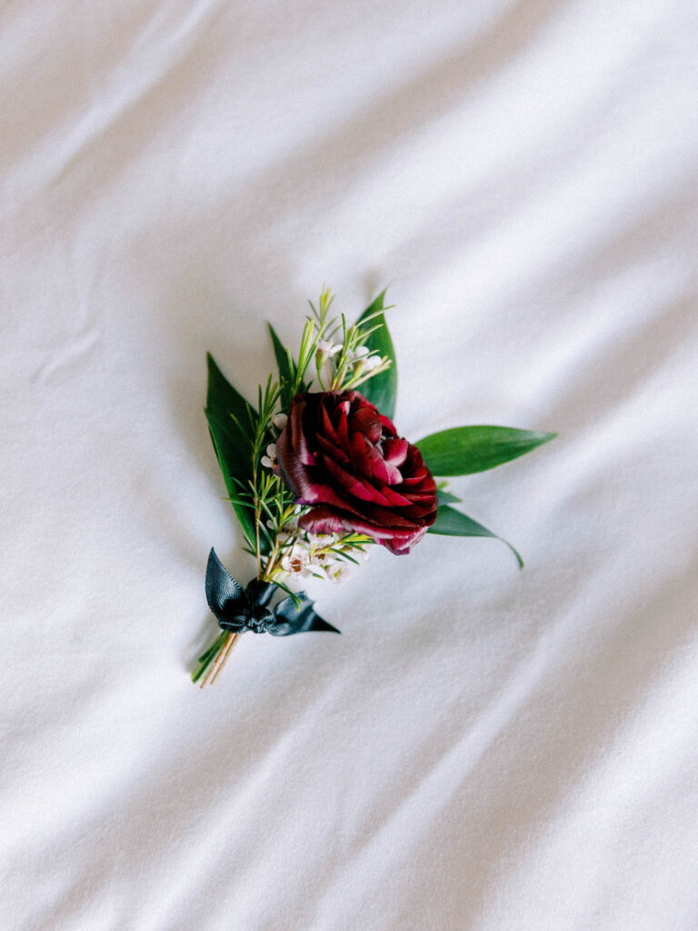 Boutonniere of maroon rose and greenery.