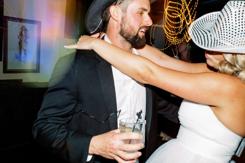 Overexposed photograph of bride and groom dancing during wedding reception with cowboy hats on.