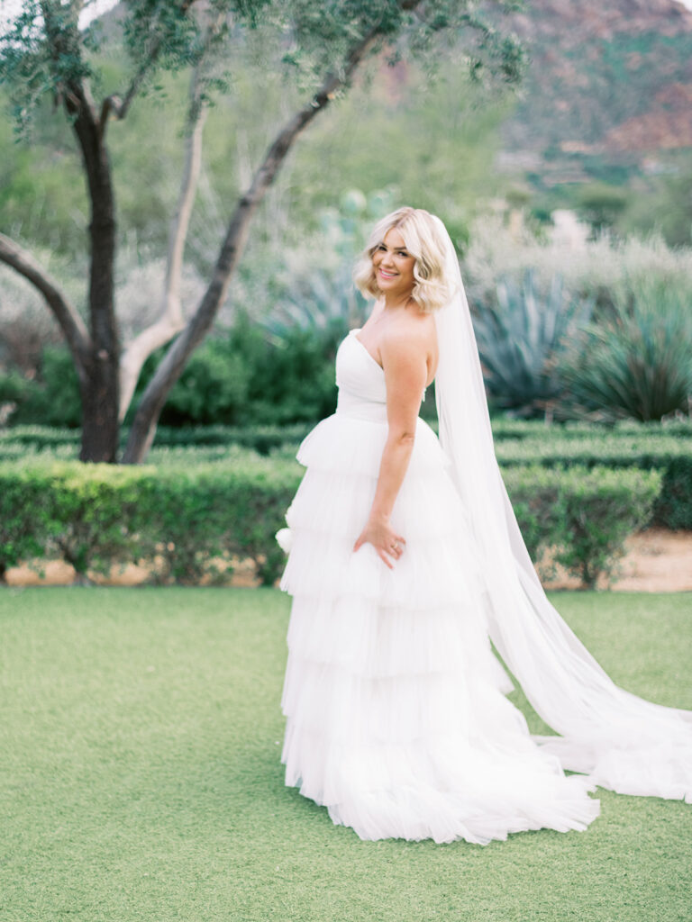 Bride smiling and looking over her shoulder standing in grass area.