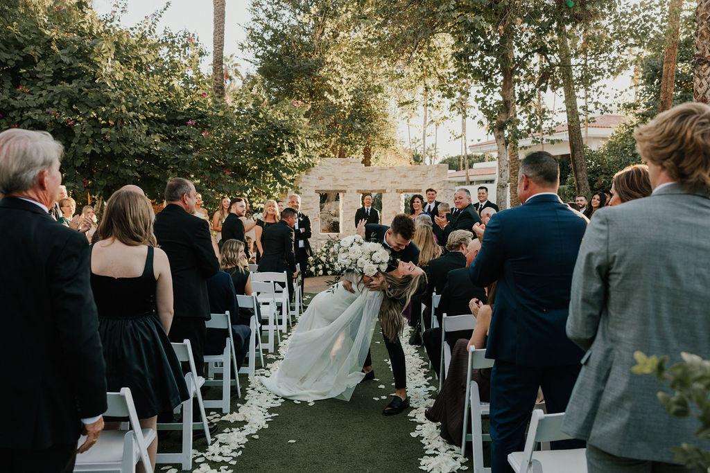 Groom dipping bride in wedding ceremony aisle white exiting.