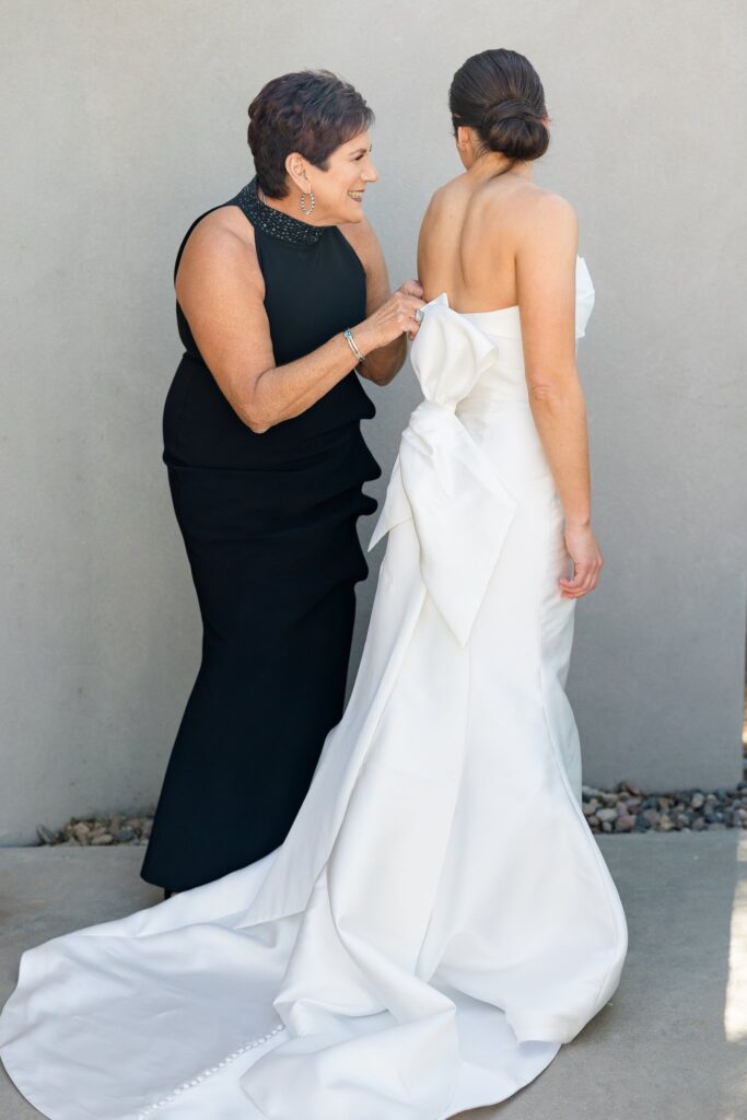 Mother helping bride get ready by zipping up the back of her dress.