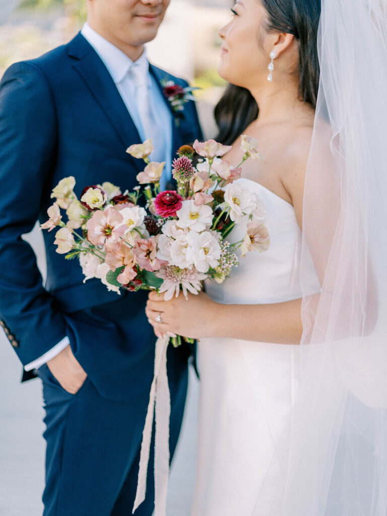 Bride and groom looking at each other, with slight smiles, bride holding bouquet.