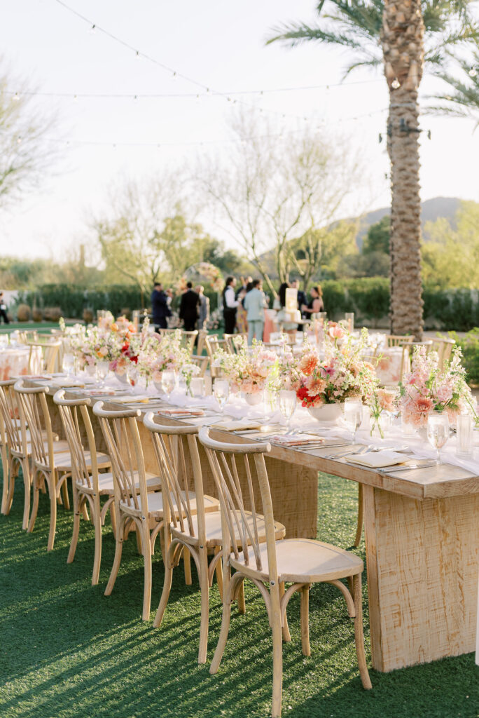 Long reception table of wood with floral centerpieces down the center in bright spring colors.