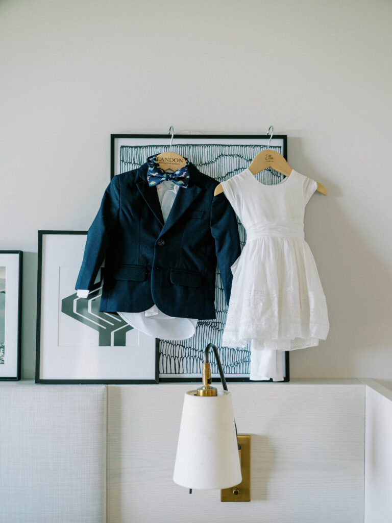 Ring bearer blue suit and flower girl white dress hanging up inside.