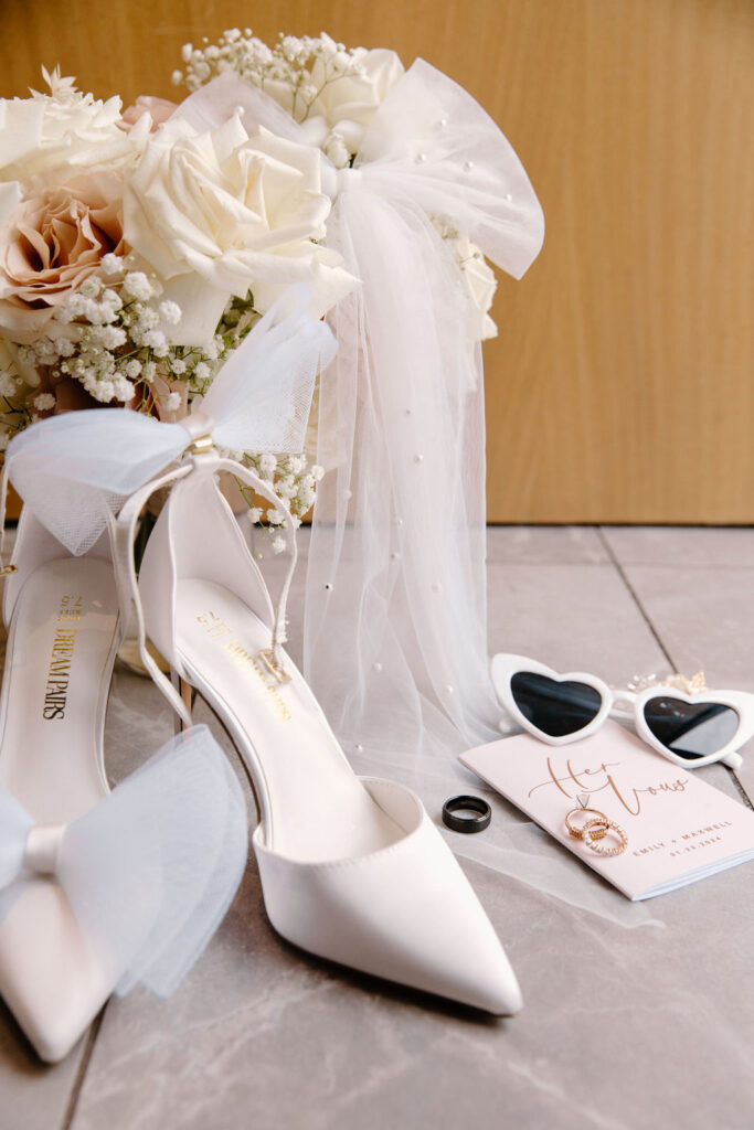 Bridal details of shoes, sunglasses, vow book, rings, and flowers.