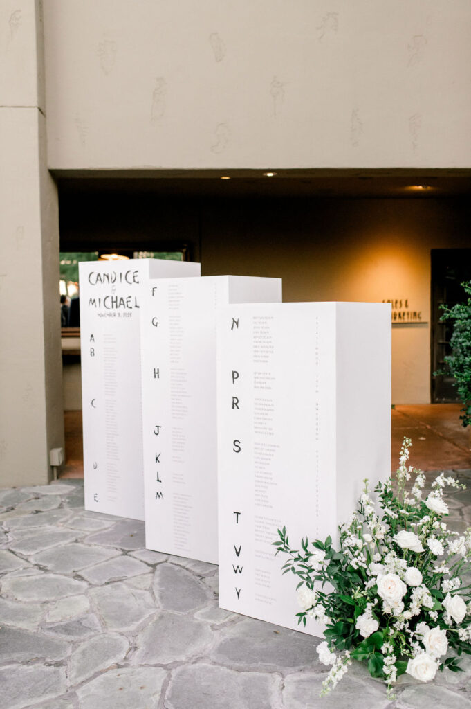 Three custom wedding escort board pillars with ground floral arrangement next to them.
