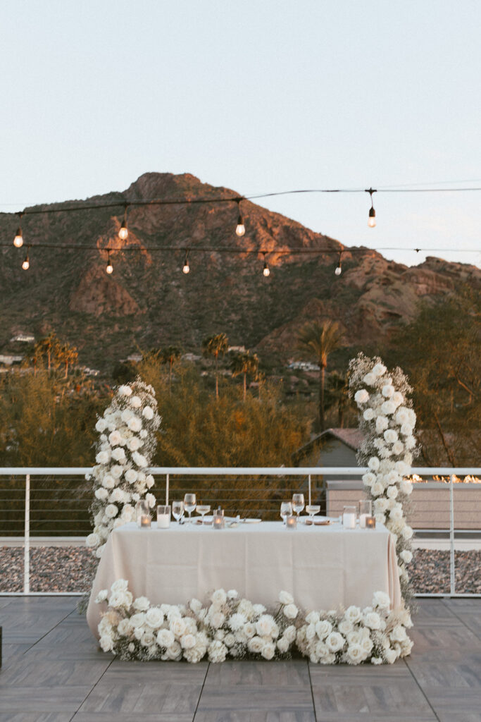 Outdoor patio reception sweetheart table with floral columns behind it and ground floral in front of it.