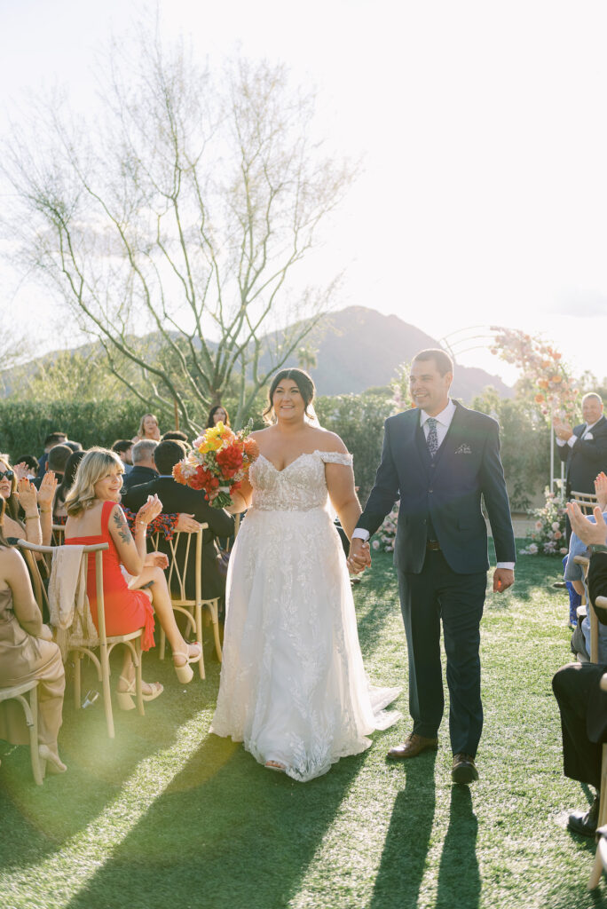 Bride and groom walking down aisle exiting ceremony holding hands.