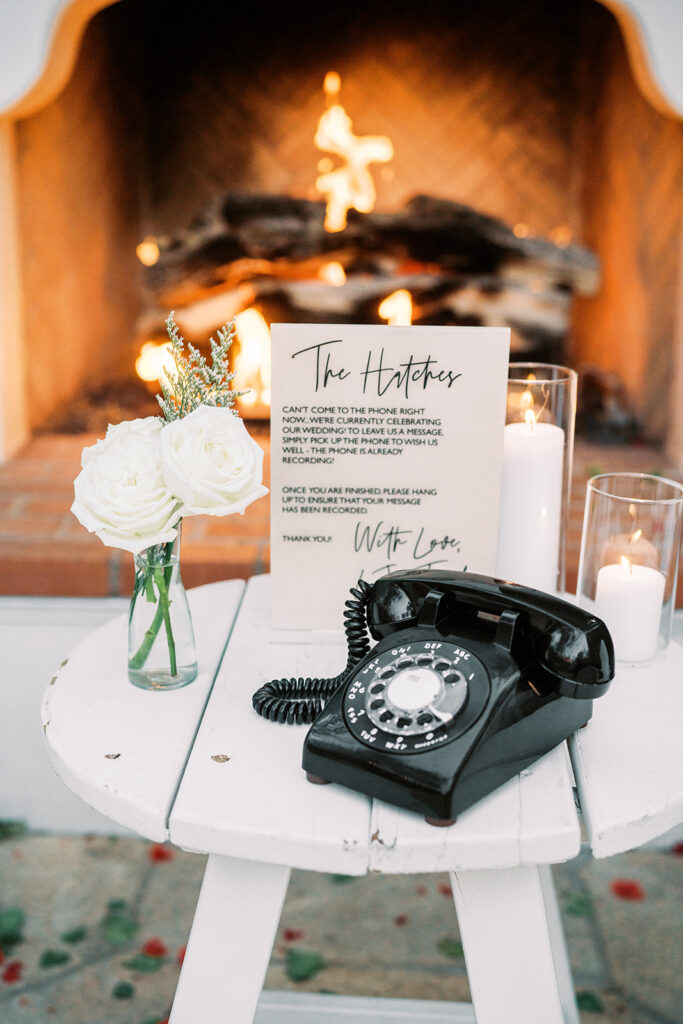 Wedding table with phone and sign, bud vase of white roses and candles.