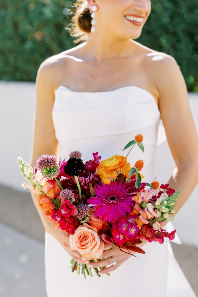 Bride holding bouquet of pink, orange, maroon, and fuchsia flowers.