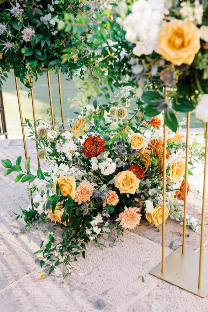 Wedding ceremony floral on ground and on gold stands.