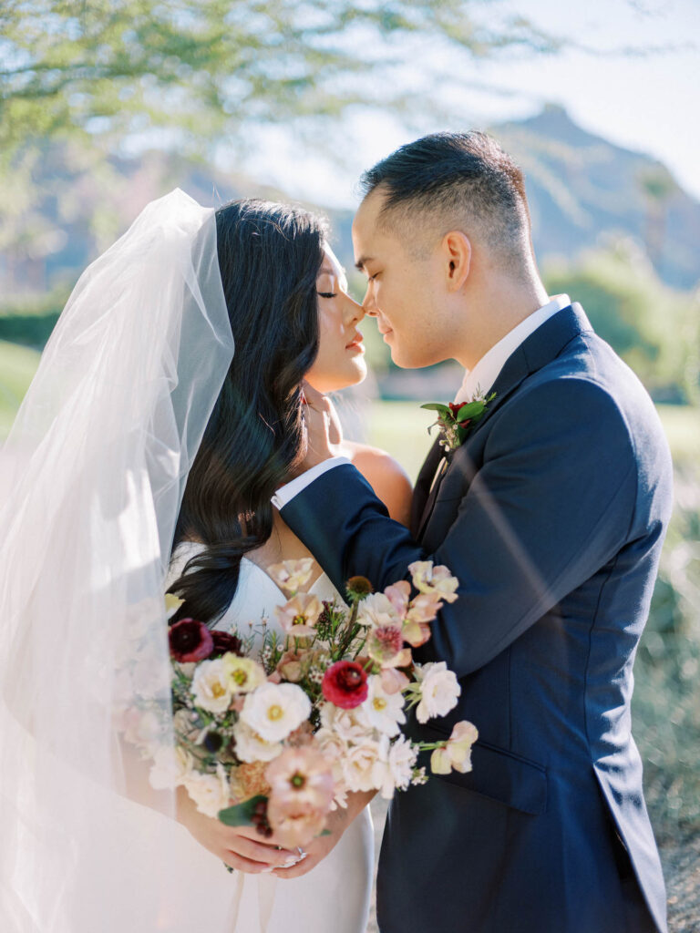 Groom softly holding bride's head while they touch noses together with eyes closed.