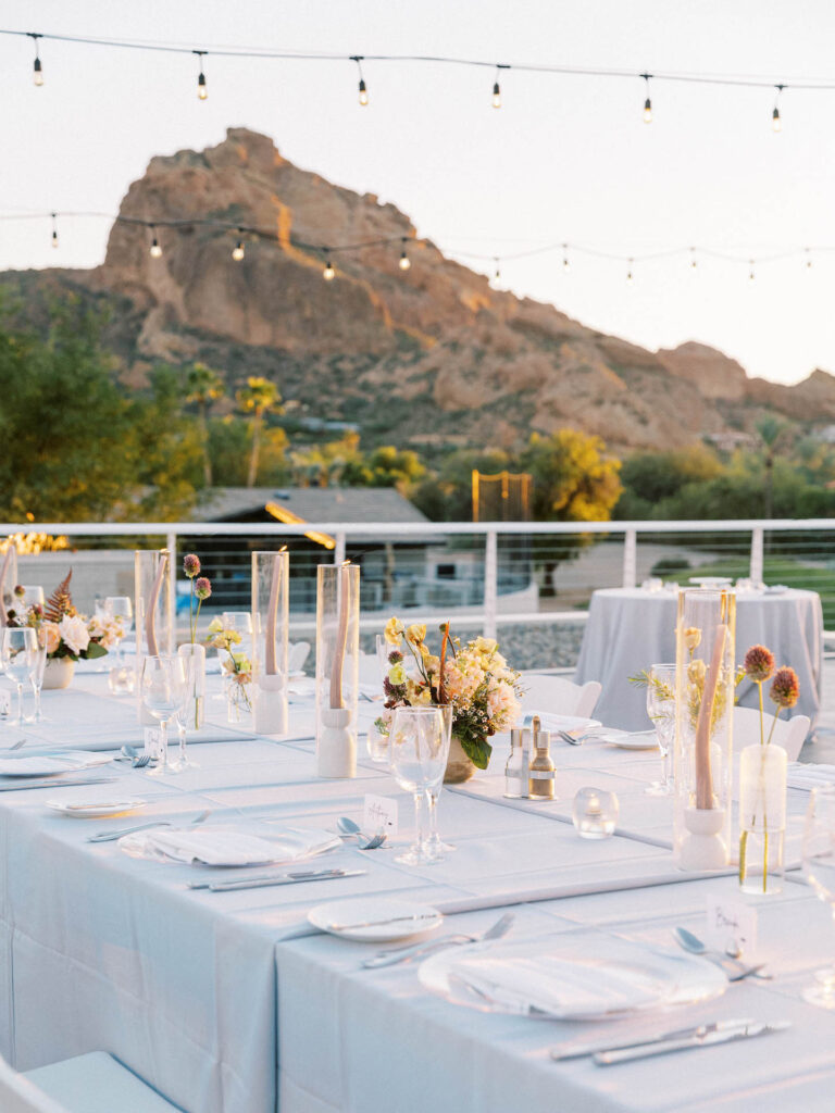 Long reception table with light gray linen, taper candles, bud vases of floral, and floral centerpieces.