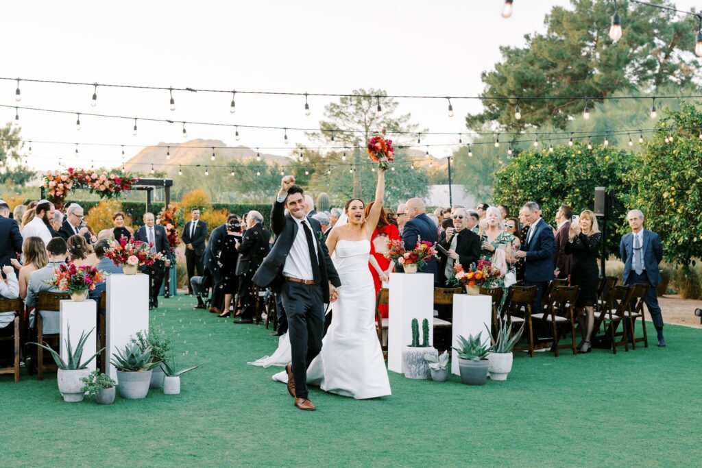 Bride and groom exiting the wedding ceremony aisle, celebrating with arms raised.