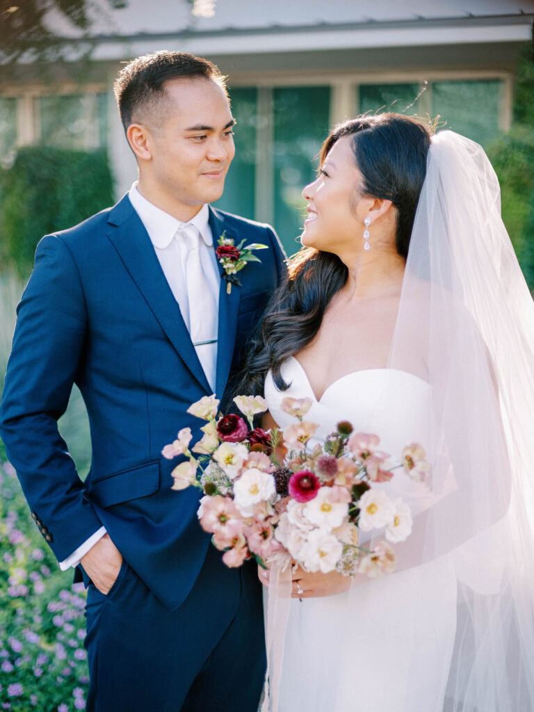 Bride and groom smiling at each other, bride holding bouquet.