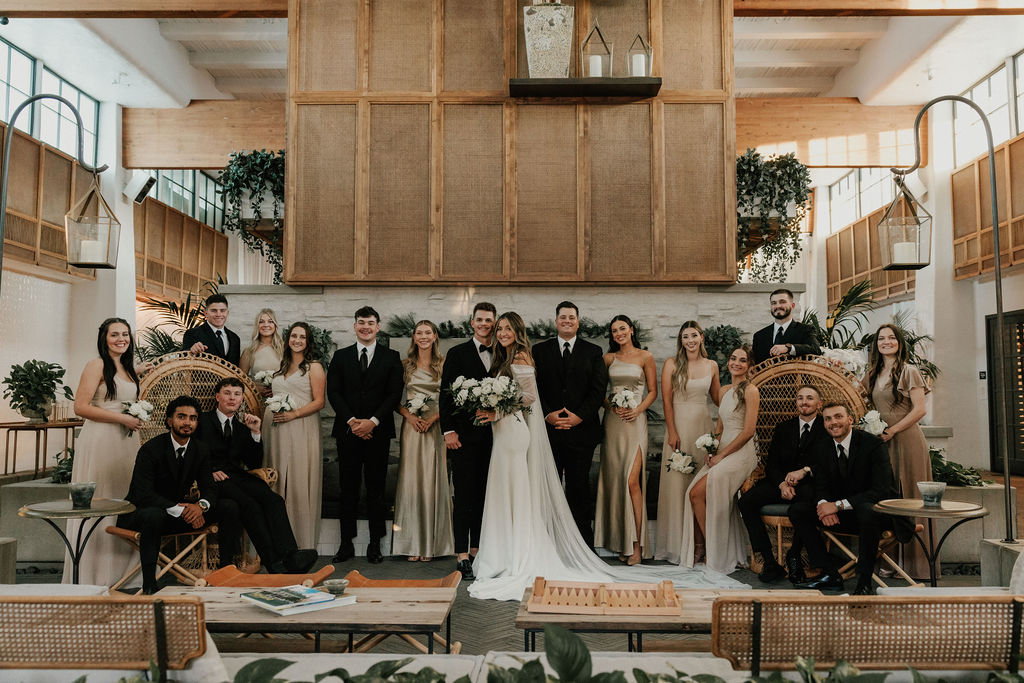 Bride and groom standing with wedding party in front of unique wall inside building with wood accents.