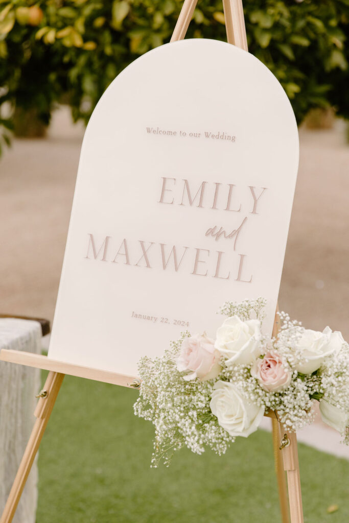 Custom welcome sign with floral added to bottom right corner of white and pink roses and baby's breath.