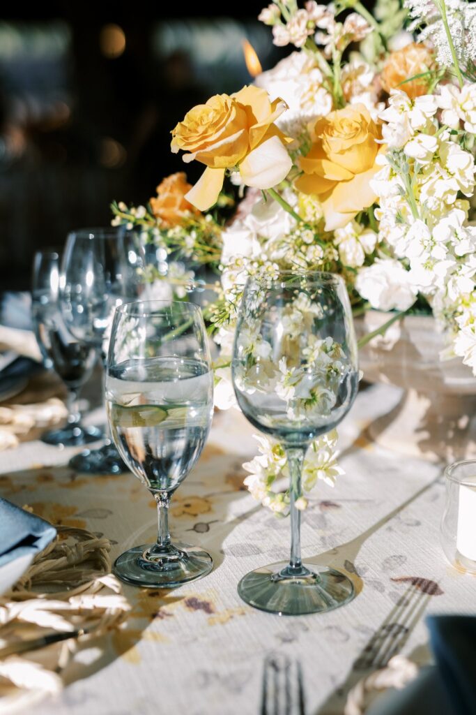 Wedding reception table blue glasses and white and gold flowers behind them.