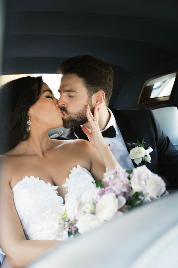 Bride and groom kissing in backseat of car.