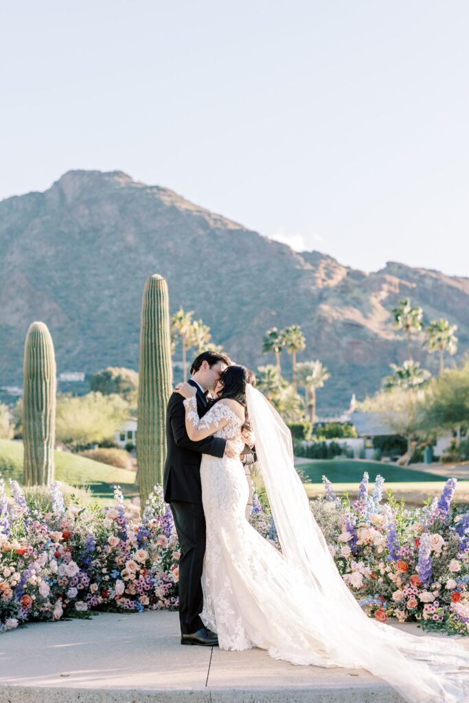 Bride and groom kissing in altar space with curved floral ground arc in altar space.