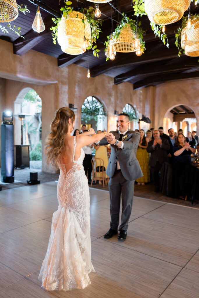 Bride and groom dancing at wedding reception on dance floor with guests around them.