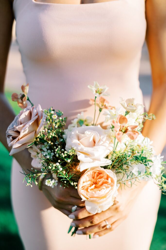 Bridesmaid in light pink dress holding roses and other flowers pink and white bouquet.