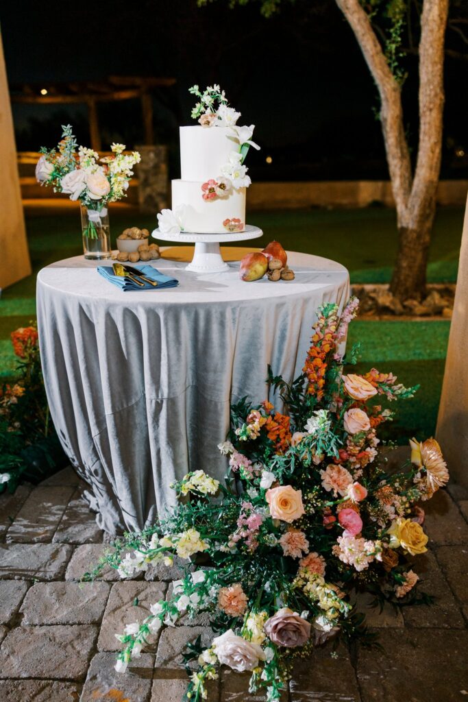 Cake table at wedding reception with flower arrangement to side on ground.