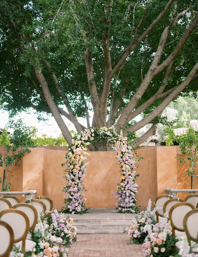 Outdoor ceremony space at Royal Palms with floral arrangements along aisle ground and floral arch in altar space.