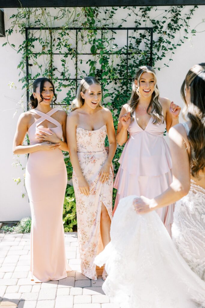 Bridesmaids having first look of bride in wedding dress, standing outside.