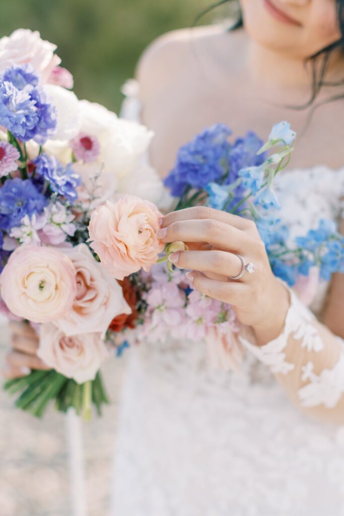 Bride gently touching pink flower in her bridal bouquet.