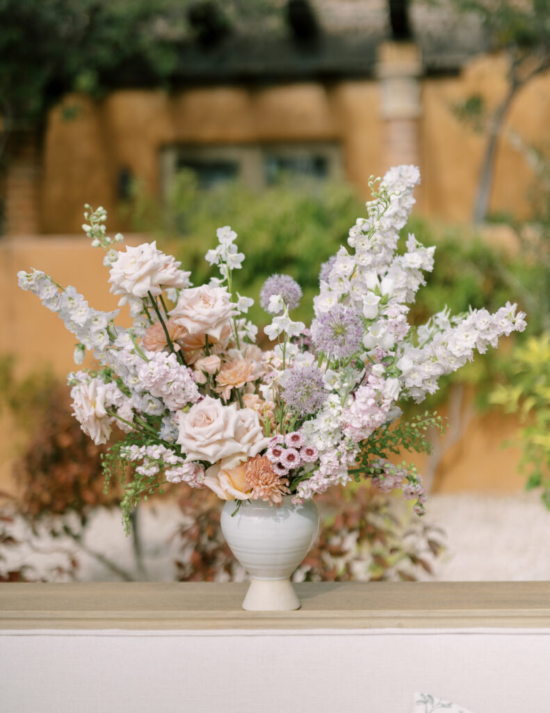 Large bar floral arrangement in neutral vase of white, purple, and blush pink flowers.