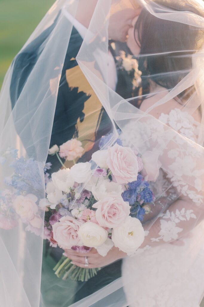 Bride and groom kissing under her veil, bride holding bouquet.