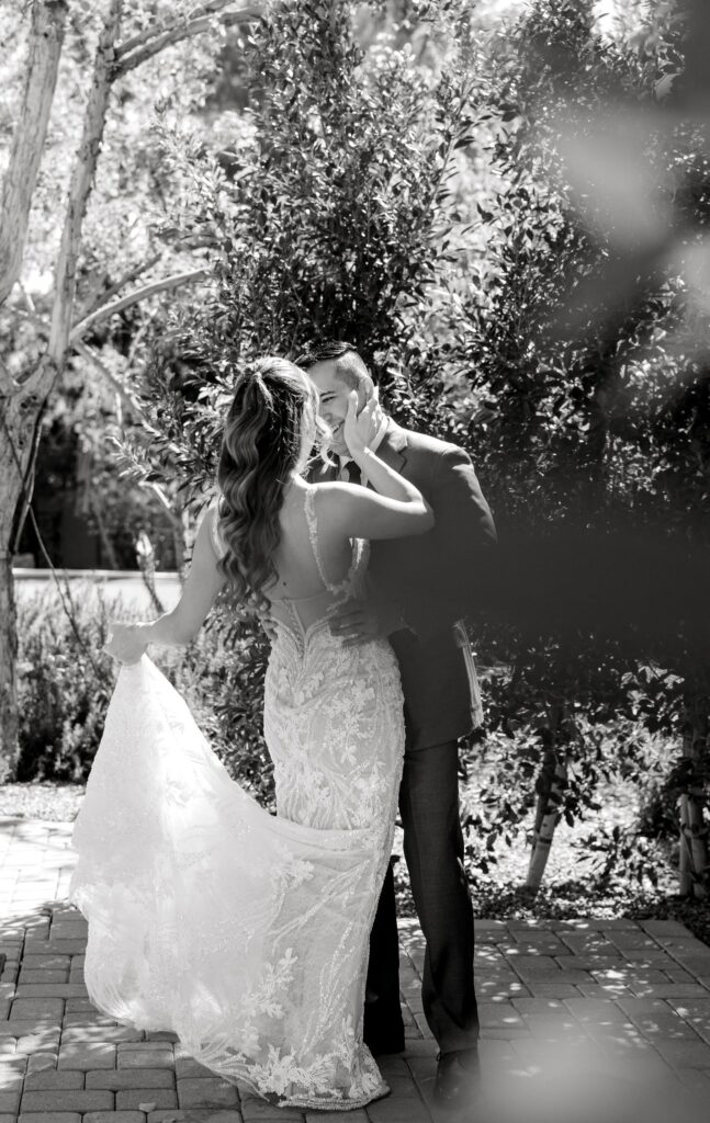 Bride with hand on groom's cheek and holding up dress train, groom smiling at her.