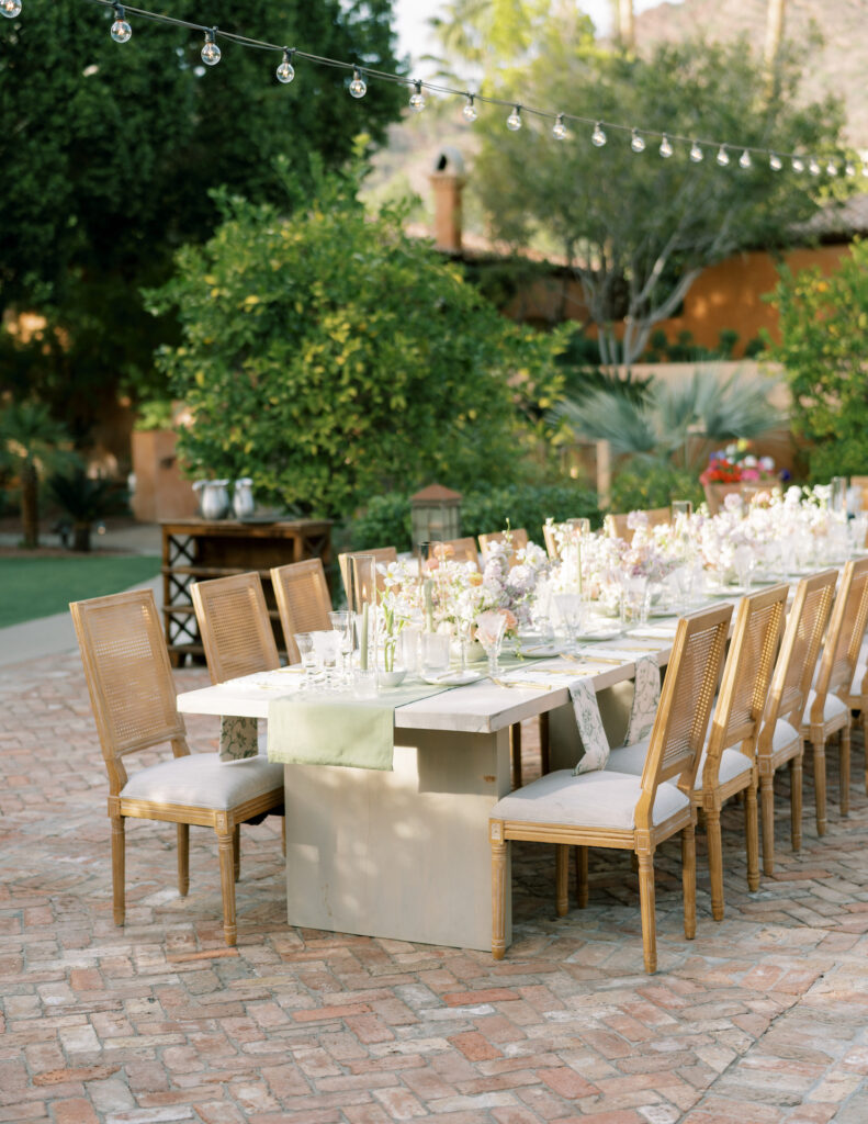 Long outdoor reception table with sage green runner in center, with floral centerpieces down center.