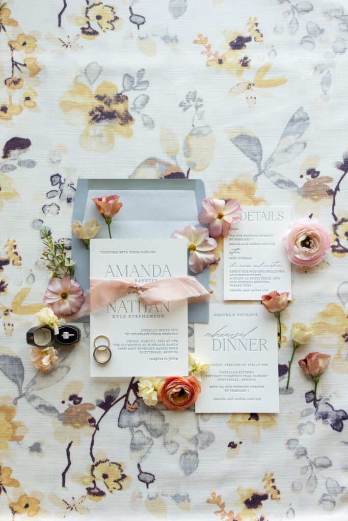 Wedding invitation flat lay of rings and flowers.