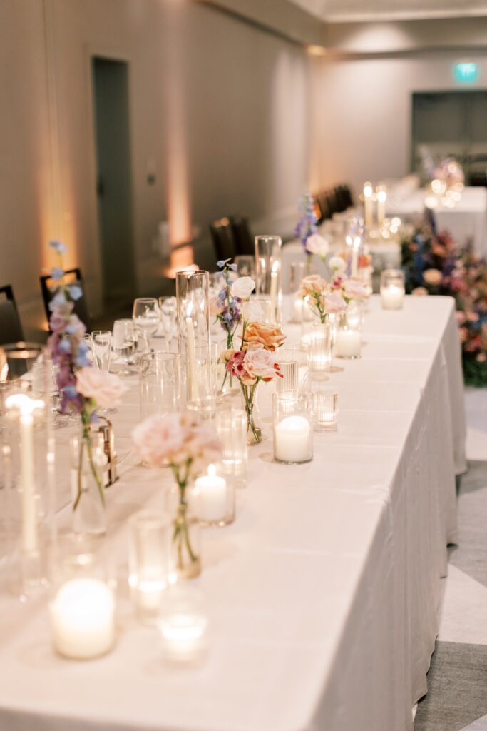 Long reception tables of bud vases and pillar candles and taper candles.